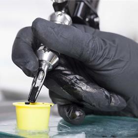 Tattoo Machine Being Dipped in Black Ink by Black Gloved Hand